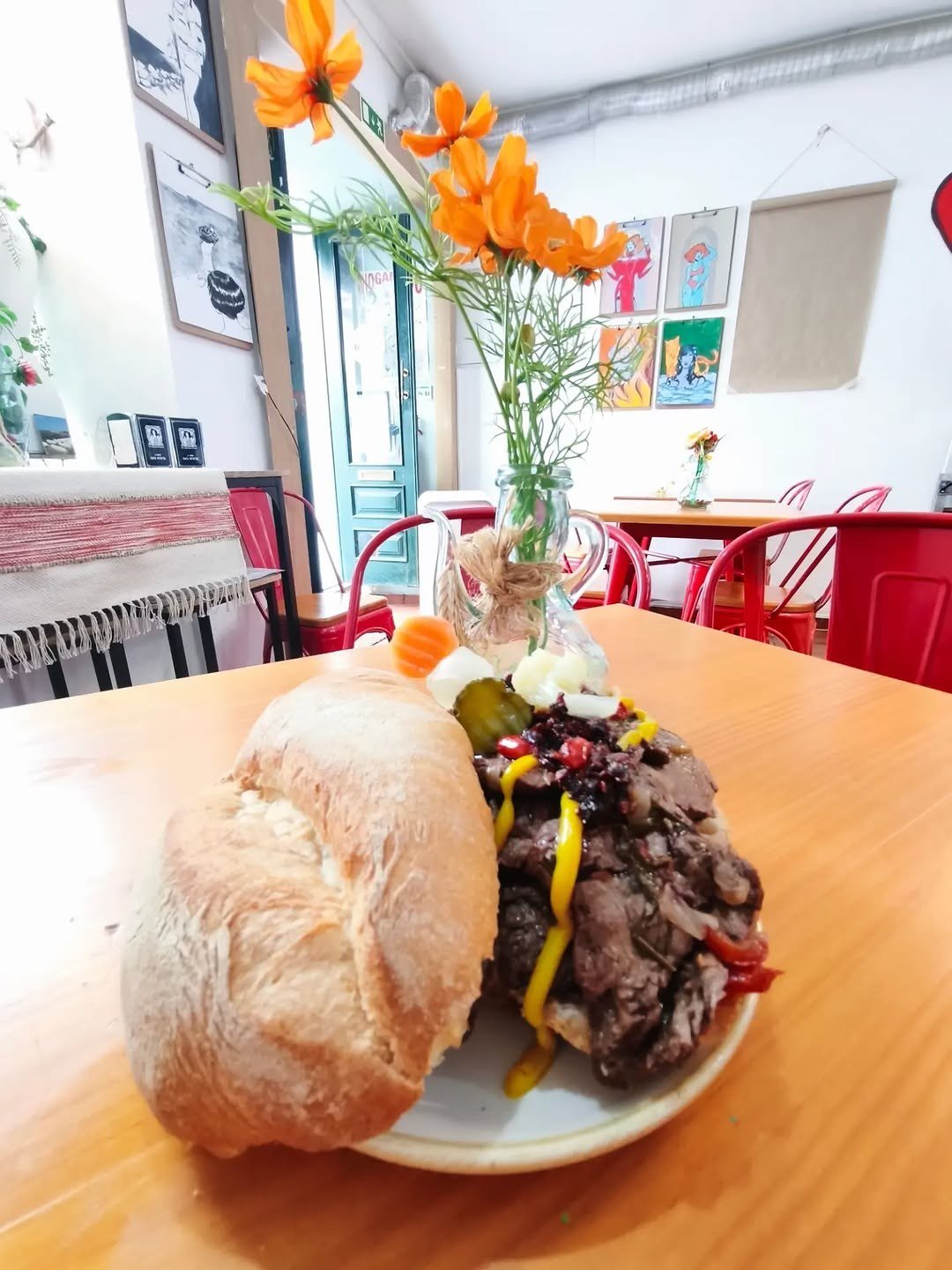 Bifana de soja em pão sobre uma mesa de madeira, com cadeiras vermelhas ao fundo
